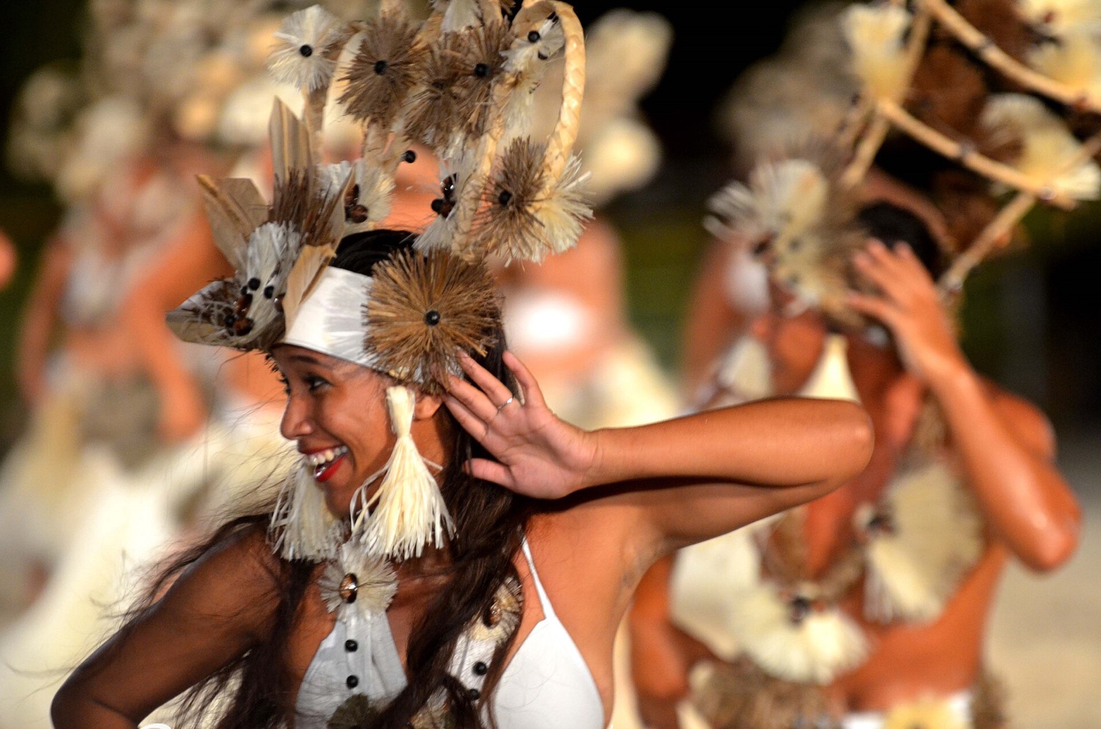 A dancer in a feather headdress performing at the Heiva i Bora Bora festival, with other dancers behind her