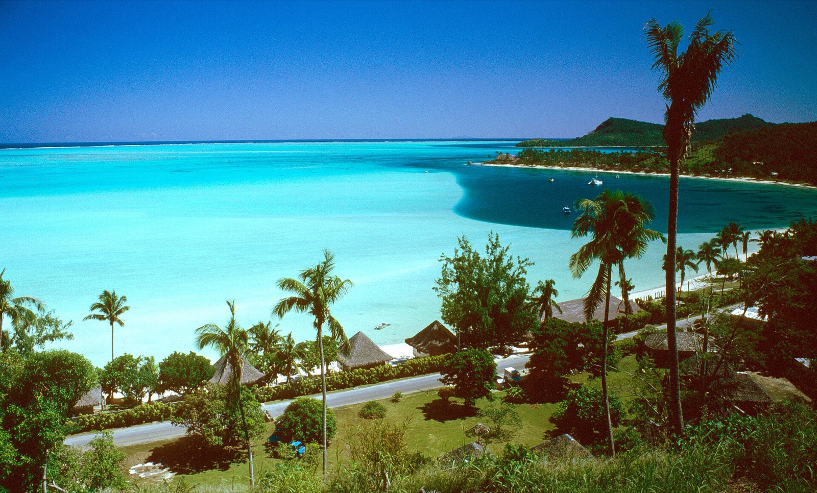 Matira Beach on Bora Bora seen from above, with palms, low roofs and the pale turquoise lagoon beyond