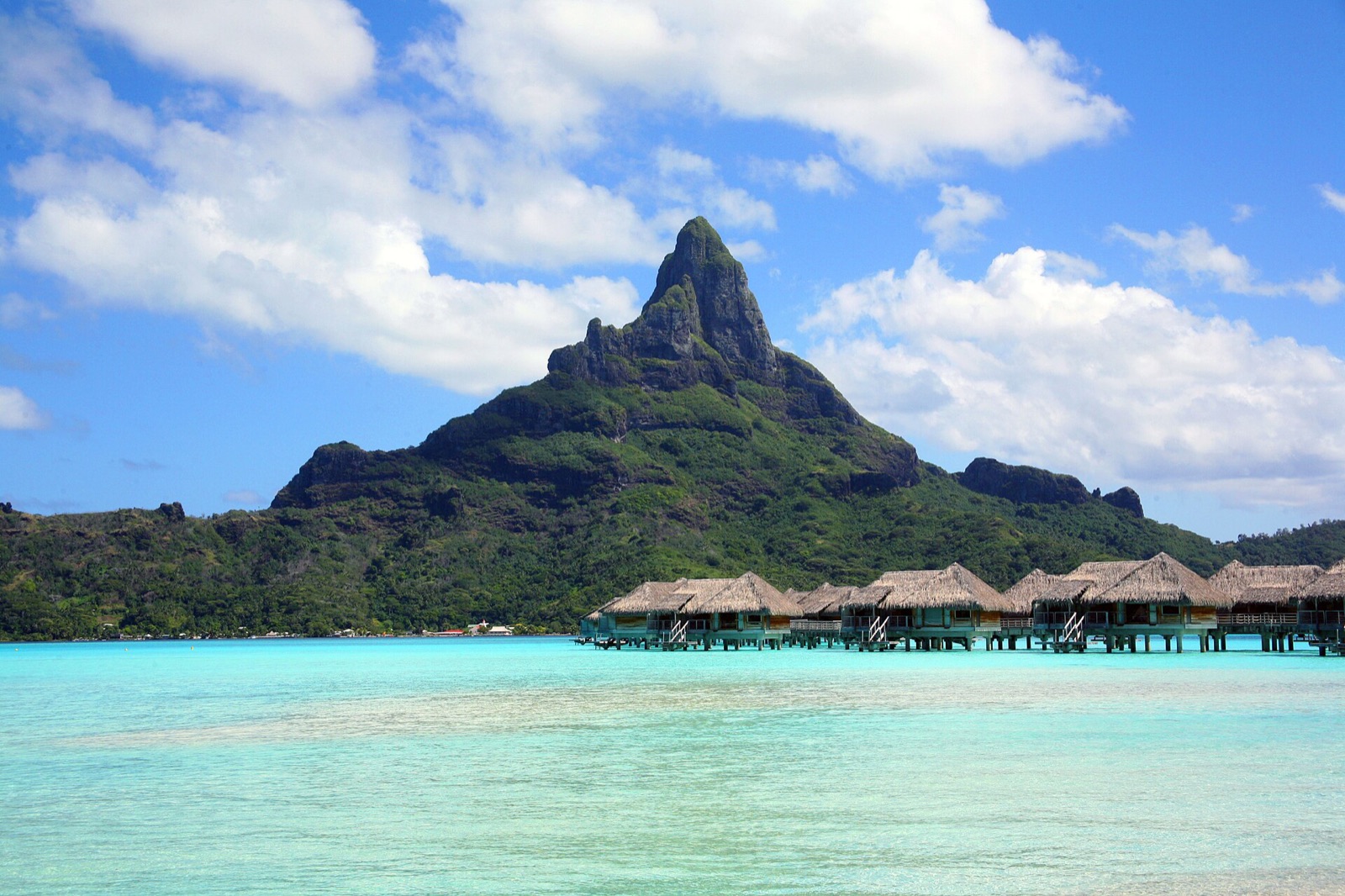 Mount Otemanu rising above the turquoise lagoon of Bora Bora, with a row of thatched overwater bungalows along the shore