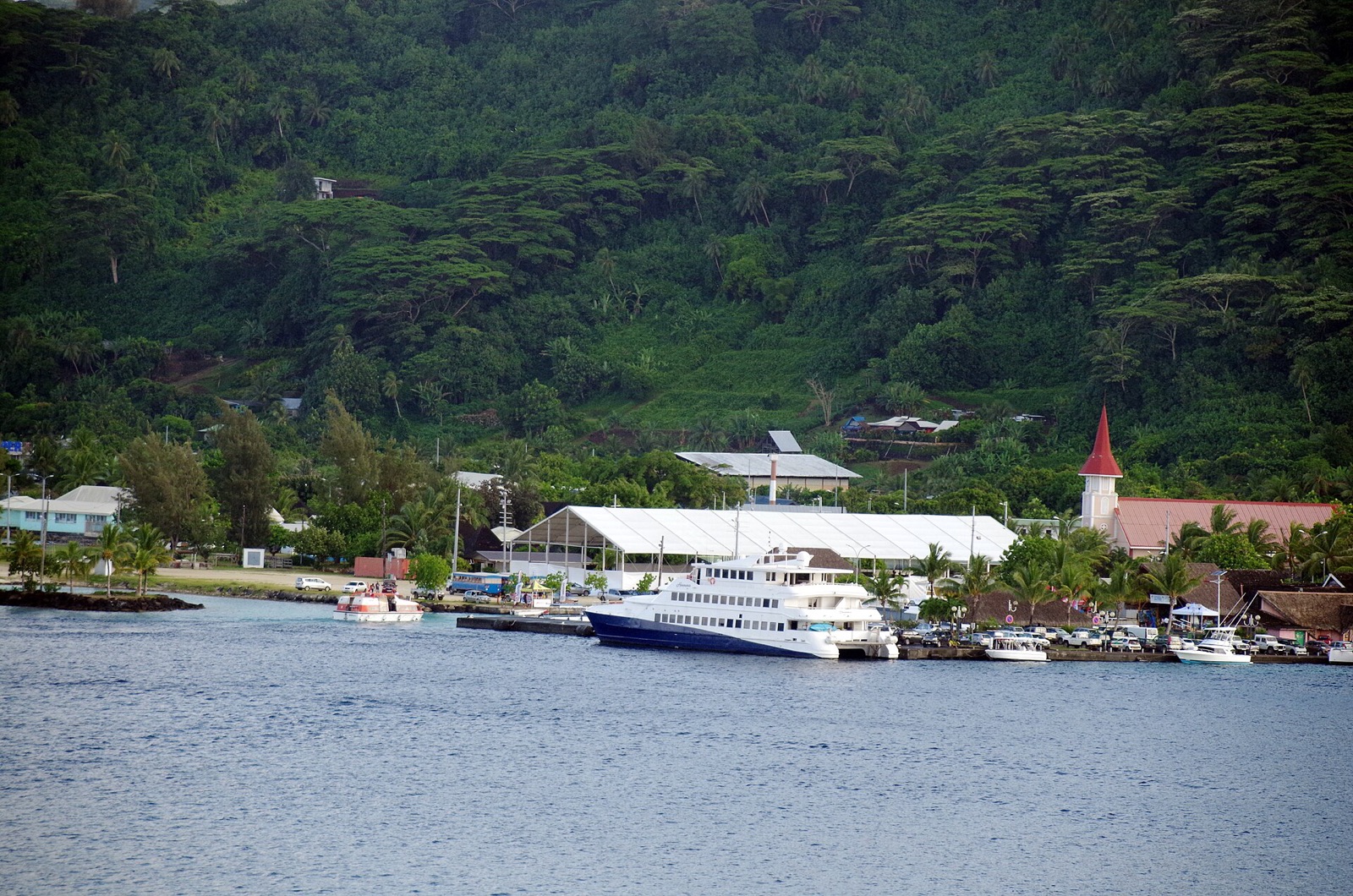 The waterfront at Vaitape, Bora Bora, with a ferry alongside the quay, the church tower and green hills behind